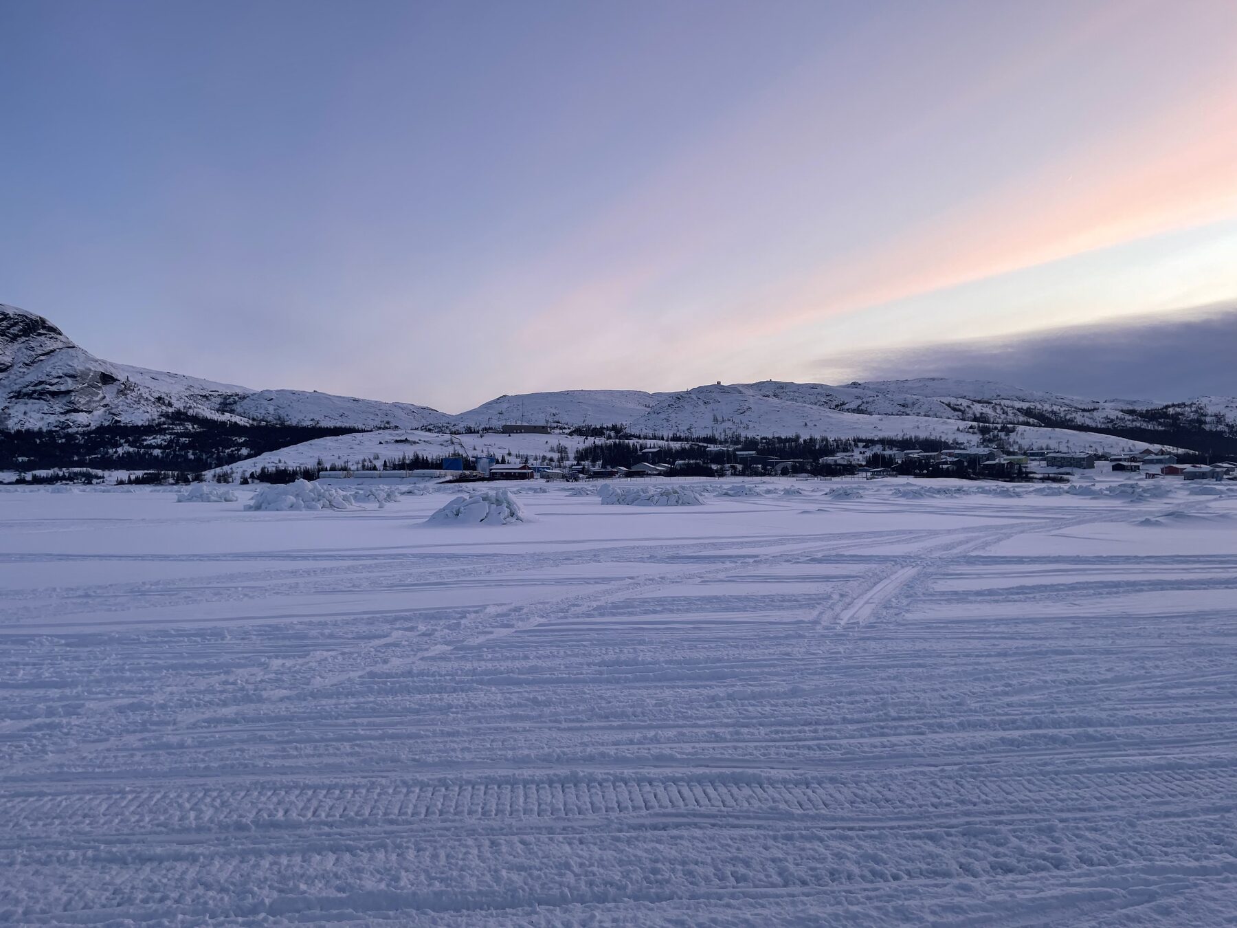 Snow-covered sea ice at dawn with mountains and a coastal community on the horizon near Nain, Nunatsiavut.